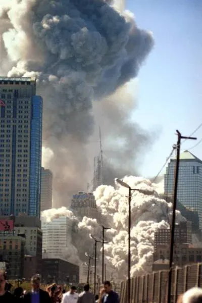 Ground-level view of WTC collapse from near the Brooklyn Bridge, pedestrians watching as a massive column of dust and smoke rises behind lower Manhattan buildings