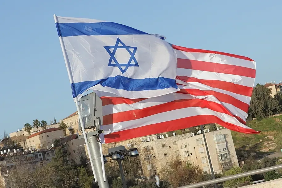 A hybrid flag combining the Star of David from the Israeli flag with the red and white stripes of the US flag, flying over Jerusalem
