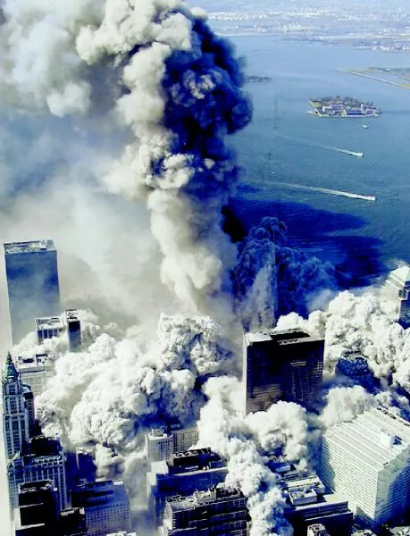 Aerial view of WTC collapse with dark blue-black smoke mixing with white dust clouds, New York Harbor and islands in background, buildings at ground level engulfed in expanding debris
