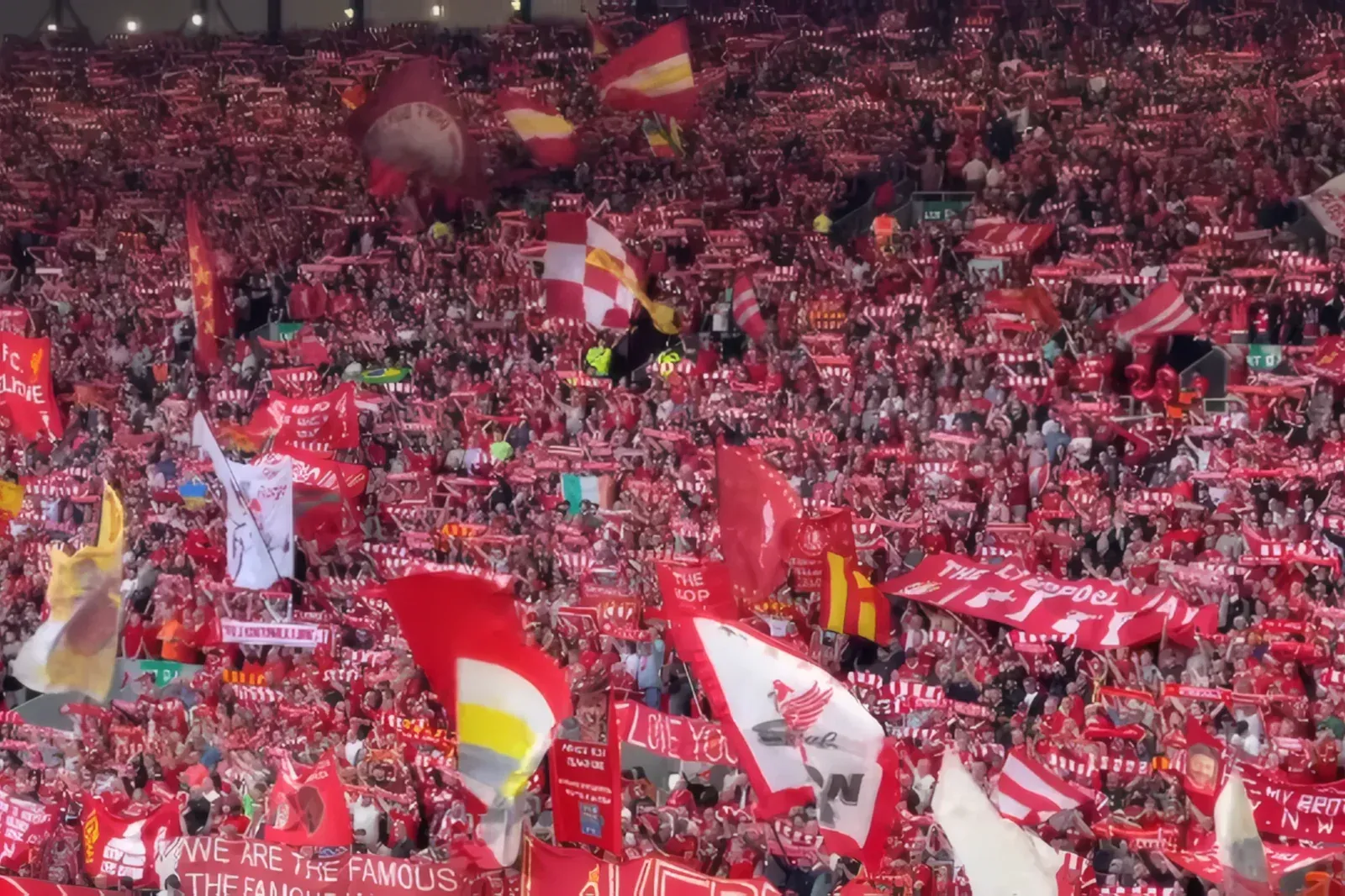 The Kop at Anfield packed with Liverpool fans holding up scarves, flags and banners in a sea of red