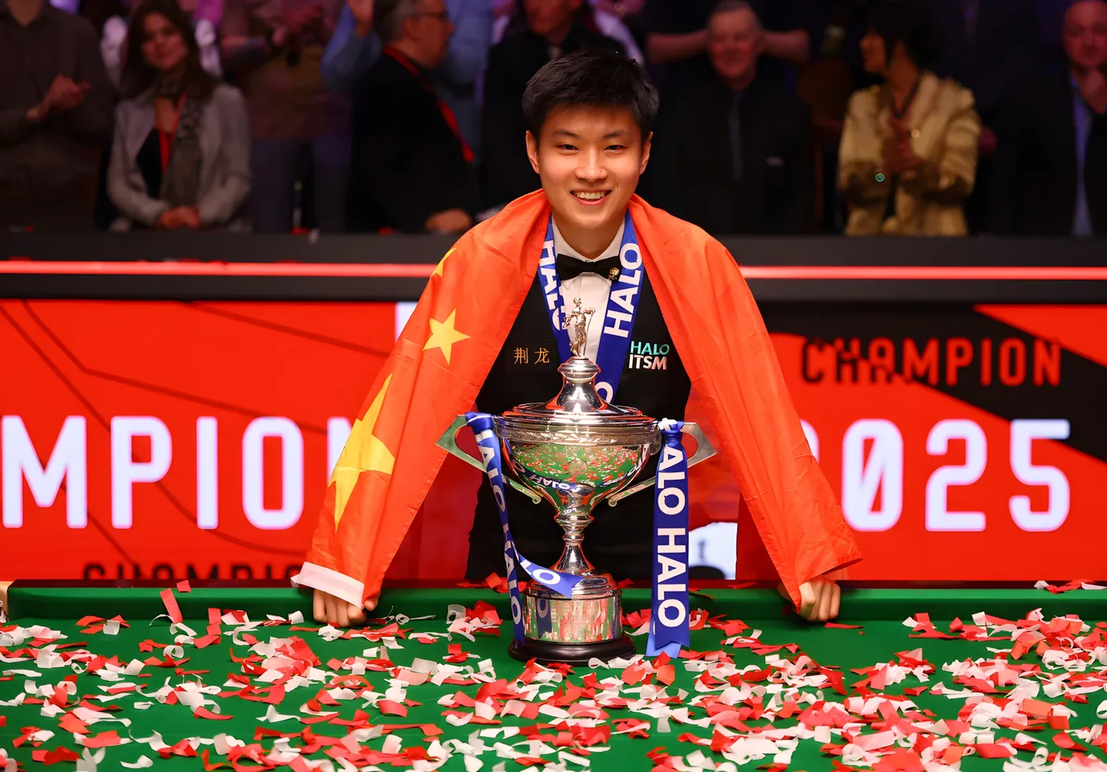 Zhao Xintong draped in a Chinese flag, smiling behind the World Snooker Championship trophy amid red and white confetti